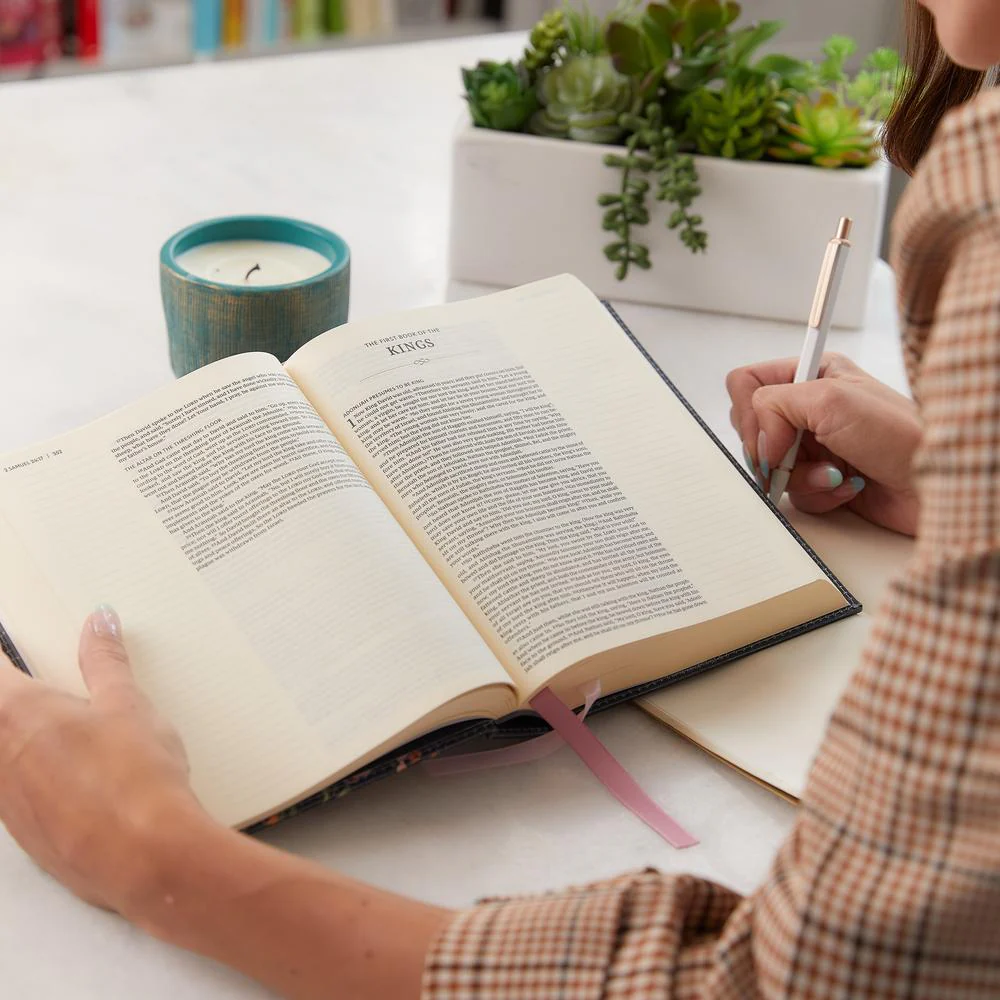 Journal the Word Bible resting on a table, a persons hands holding a pen illustrating journaling while reading Scripture.
