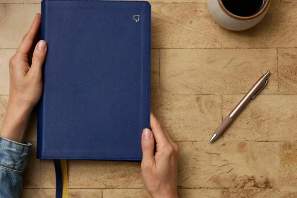 Person preparing to open NET Bible Full Notes Edition with blue Leathersoft cover on a wooden table top