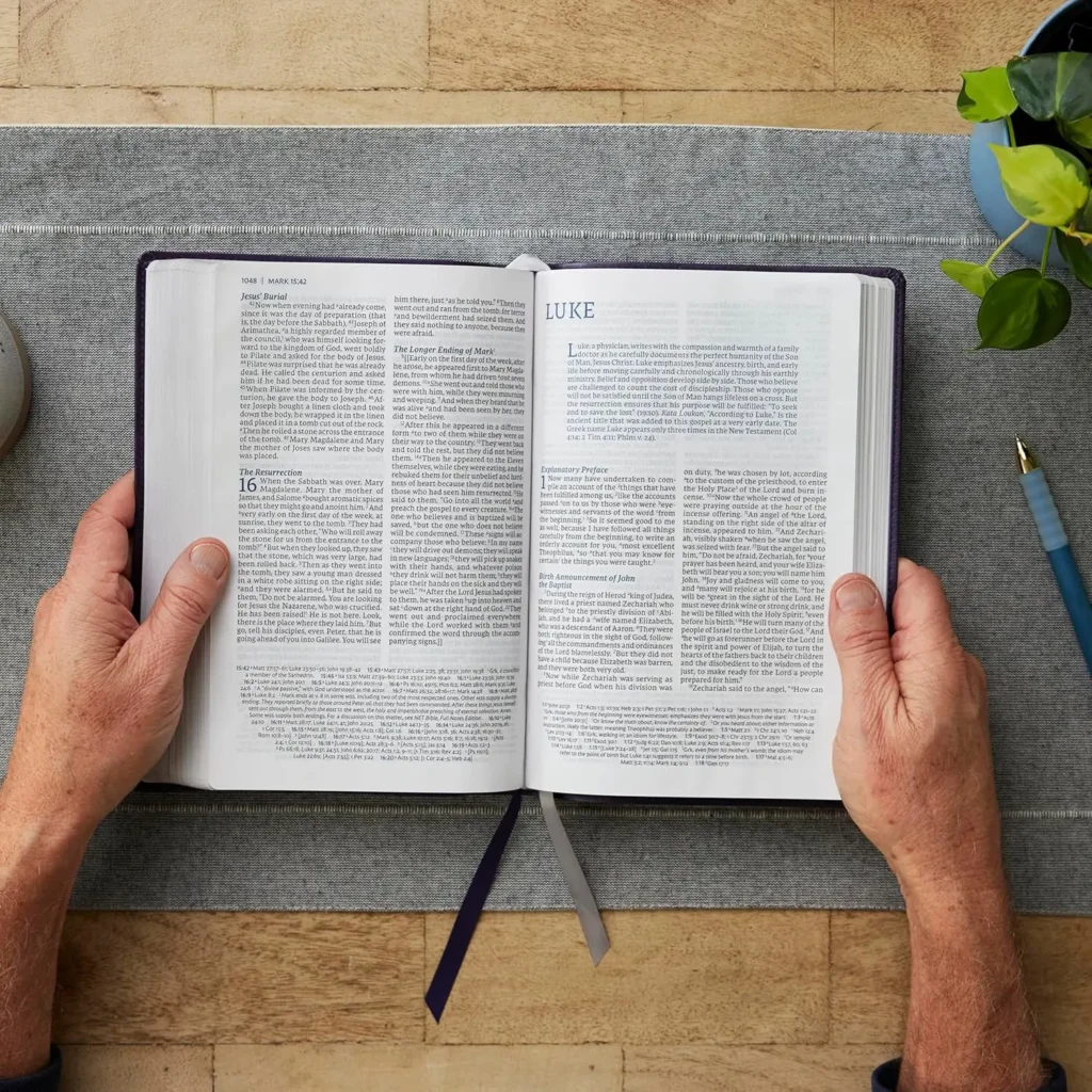 NET Thinline Reference Bible open on a table, a persons hands holding the pages open to the Gospel of Luke