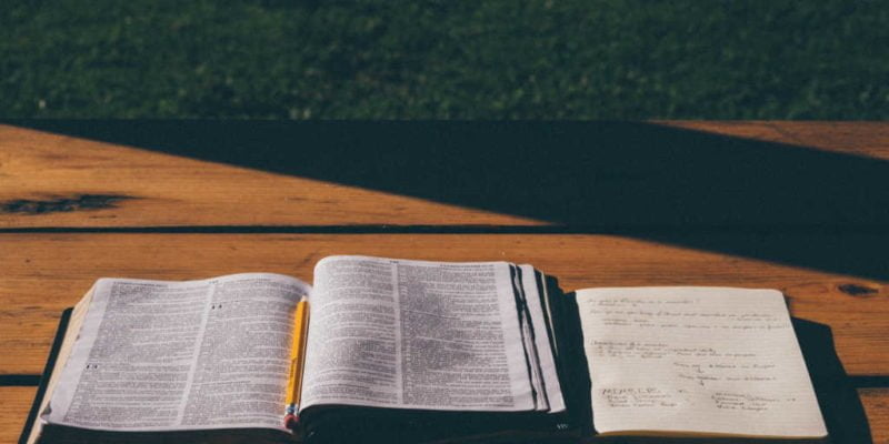study bible and notebook open on outdoor wooden table