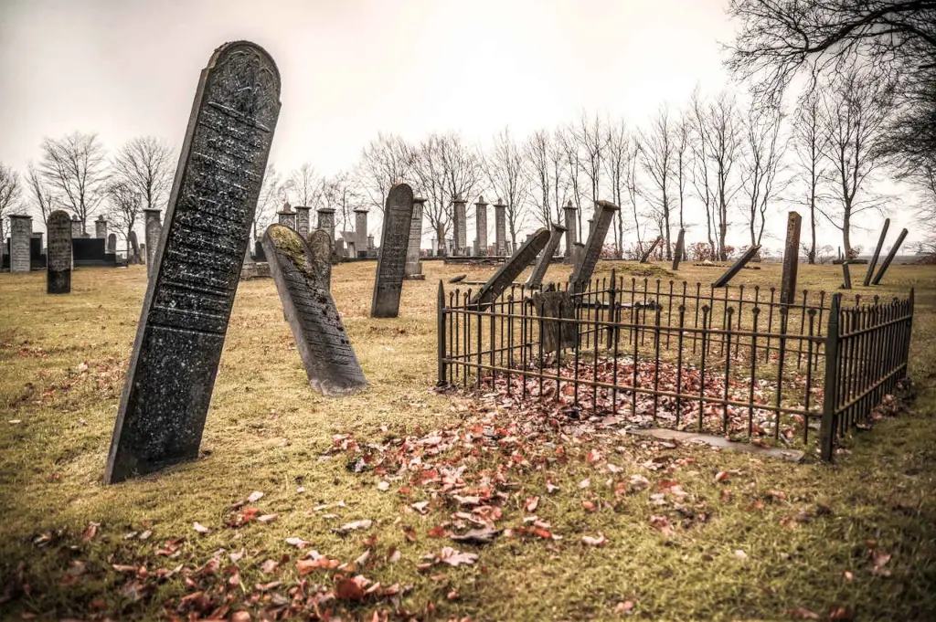 Old cemetery with leaning gravestones and barren trees creating a bleak, unsettling atmosphere often associated with death and the spiritual darkness portrayed in horror films.