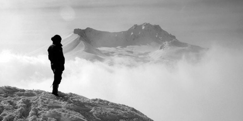 man looking at valley filled with fog from mountain top