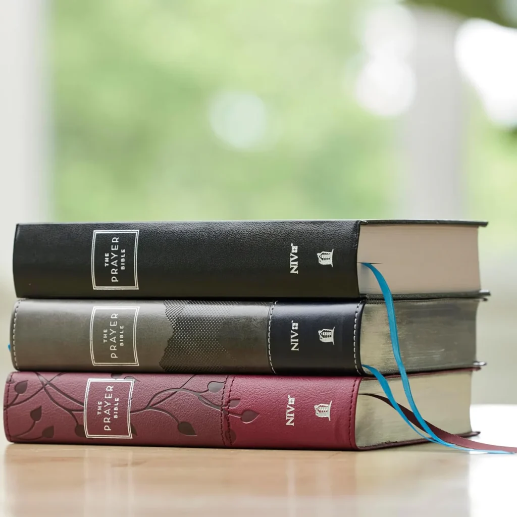 The Prayer Bible NIV hardcover and Leathersoft editions stacked on a wooden table